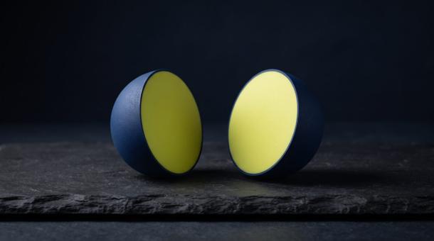 A navy sphere cut cleanly in half, both halves resting on dark slate with the chartreuse cut faces turned to camera.