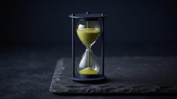 A slender hourglass with a navy frame standing on dark slate, the sand running through it bright chartreuse.