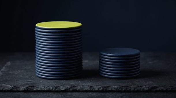 Two stacks of navy discs on dark slate, the left stack noticeably taller, its topmost disc chartreuse.