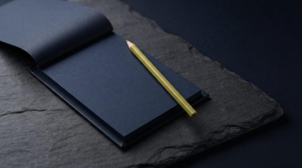 A navy order pad lying open and completely blank on dark slate, a single chartreuse pencil resting across it.
