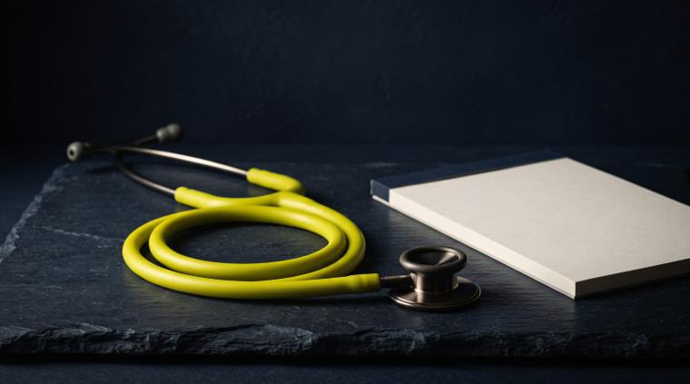 A stethoscope coiled on navy stone beside a blank prescription pad