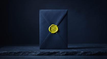 A sealed envelope standing upright on navy stone, its wax seal catching the light