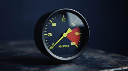 An analogue pressure gauge on navy, its needle deep in the red zone