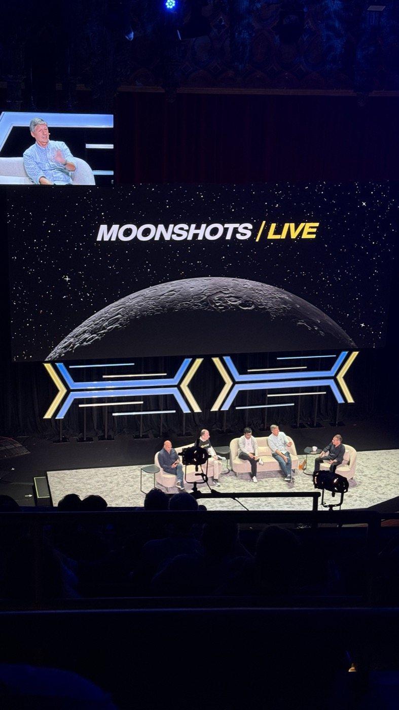 The auditorium of the United Theater from the seats, a panel on stage under the Moonshots Live screen.