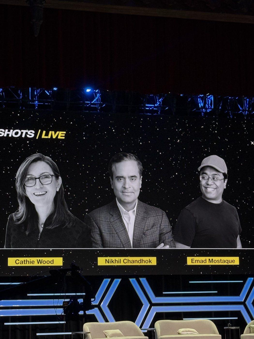 The screen shows the panel title card with the names Cathie Wood, Nikhil Chandhok and Emad Mostaque.