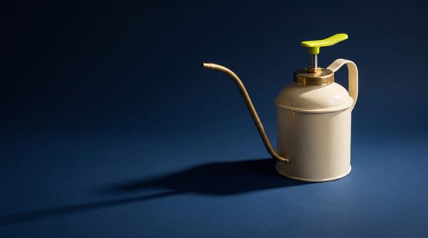 A cream enamel oil can with a long brass spout standing on smooth navy, its pump handle enamelled acid yellow-green, throwing one long hard shadow.