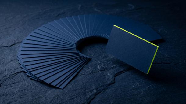 An arc of blank navy cards fanned out on stone, one card lifted clear of the row with an acid yellow-green edge catching the light.