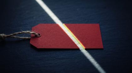 A red discount price tag cut in half by a blade of light on dark navy stone