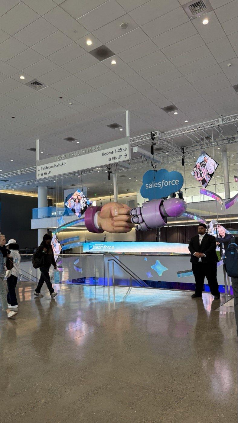 A sculpture of a human hand and a robot hand bumping fists stands under the Salesforce logo.