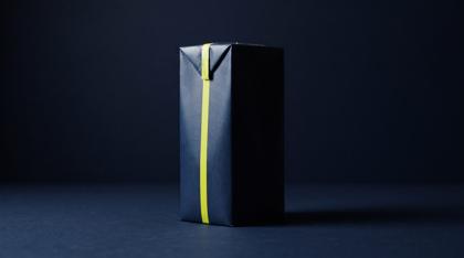 A plain unlabelled juice carton on navy, half lit and half in deep shadow