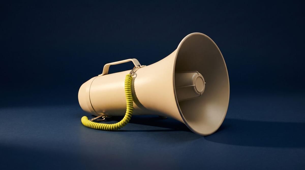 A cream metal megaphone lying on its side on a smooth navy surface, a coiled acid yellow-green cord looped from its handle, lit hard from one side