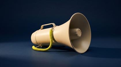 A cream metal megaphone lying on its side on a smooth navy surface, a coiled acid yellow-green cord looped from its handle, lit hard from one side