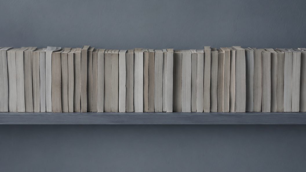 A library shelf packed end to end with paperbacks all shelved backwards, so only their worn page edges face out and no title is visible