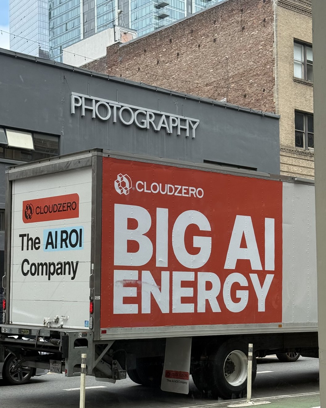 A box truck parked on a San Francisco street, its side painted bright red with the words BIG AI ENERGY in white, the CloudZero logo above it and The AI ROI Company on the cab, under a grey building whose sign reads PHOTOGRAPHY