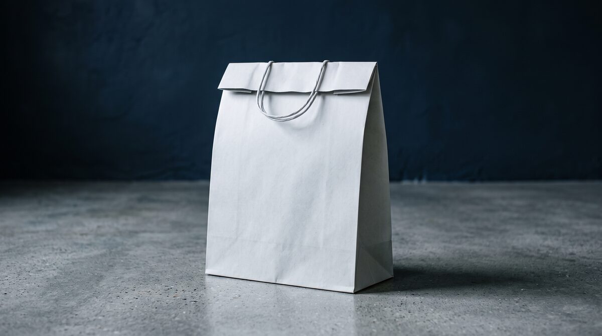 A plain paper carrier bag with no logo, lit against a deep navy wall: the version of shopping that starts online and ends with someone checking the product in person.