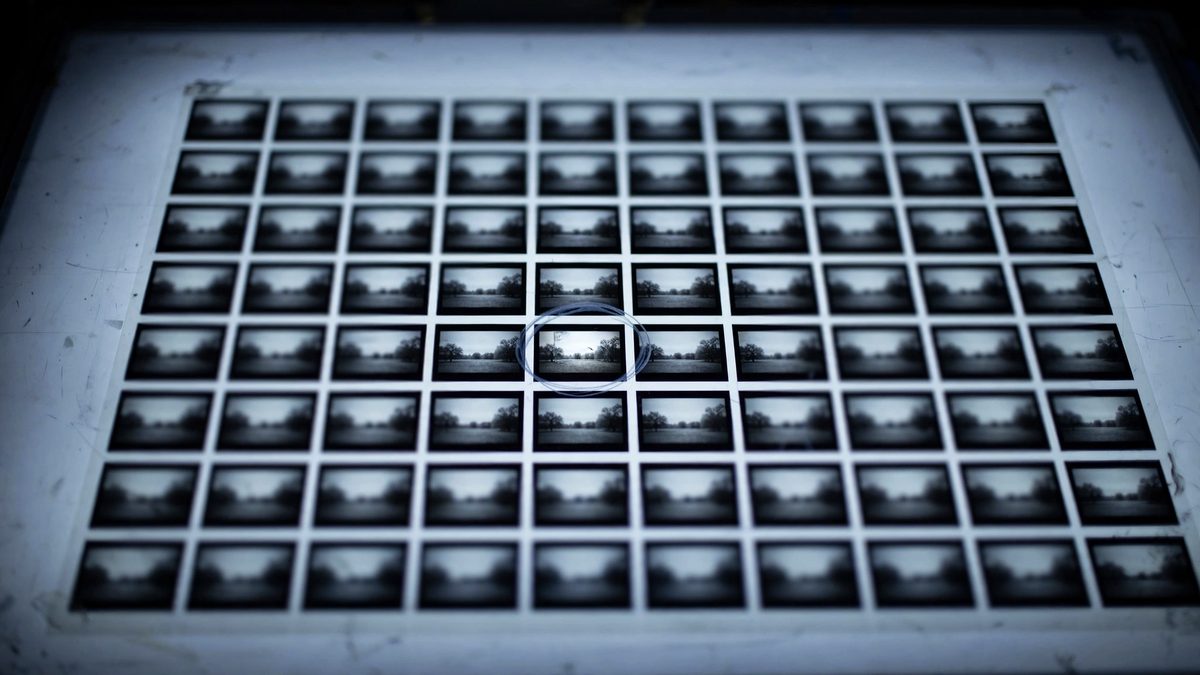 A photographic contact sheet on a light table, dozens of near-identical frames, one of them ringed by hand
