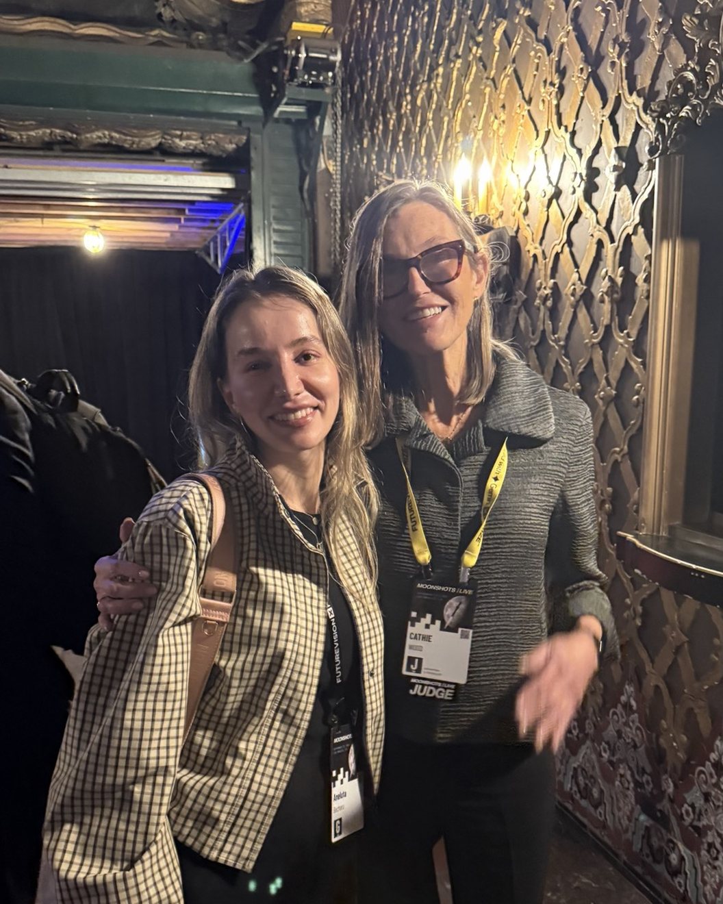 Anne Becheru and Cathie Wood side by side in the ornate lobby of the United Theater, Cathie Wood wearing a Moonshots Live judge badge