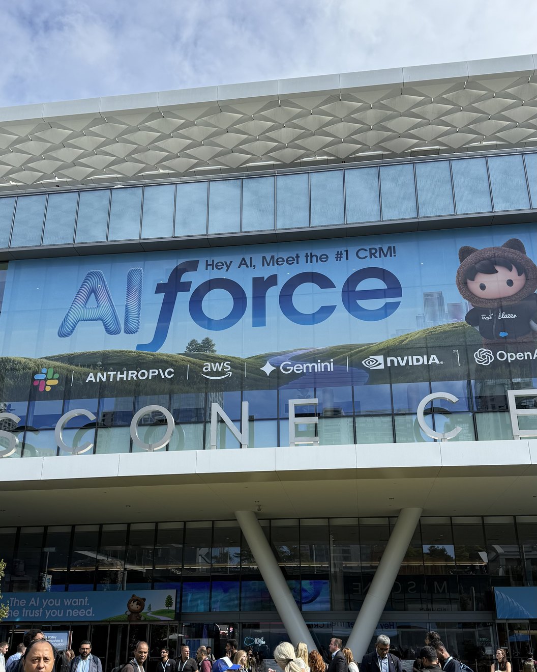 The Moscone Center frontage under a wide banner reading AIforce and Hey AI, Meet the number one CRM, with a row of partner logos beneath it and a crowd of attendees on the lawn below