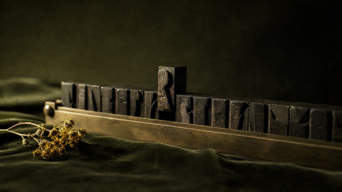 Worn wooden letterpress type blocks in a brass composing stick, one block lifted out of line, on dark olive velvet